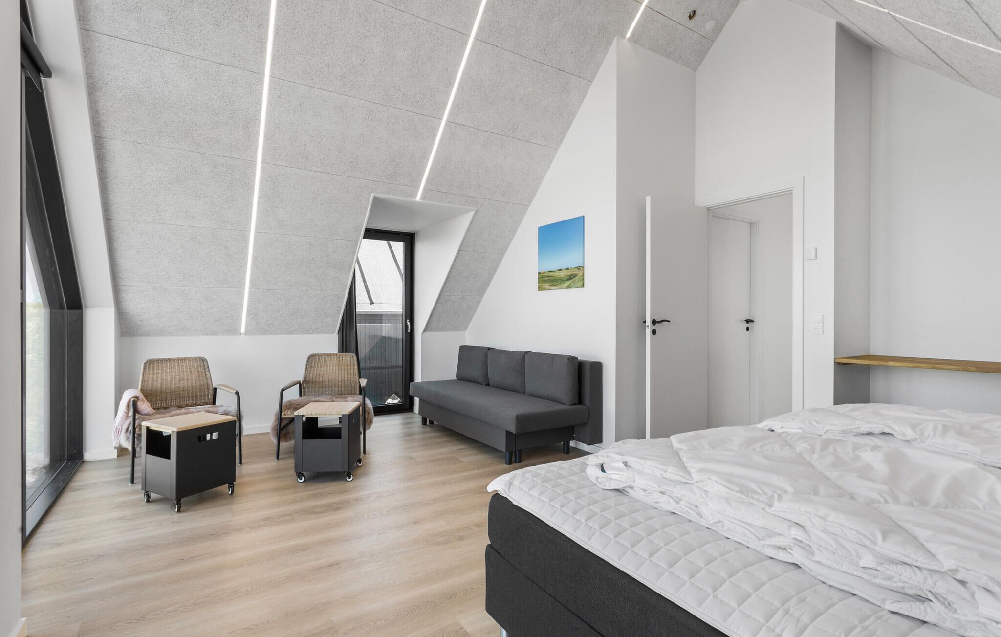 A modern bedroom with a loft-style ceiling, a bed, a sofa, and two chairs.