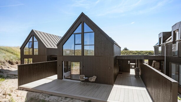 Una casa moderna frente a la playa con terraza de madera y grandes ventanales.