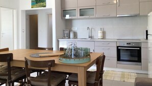 A modern kitchen with a dining area, featuring a wooden table, chairs, a coffee maker, and a built-in oven. - Beautiful home in Sukosan (Sukosan)
