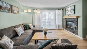 Ein Wohnzimmer mit Ecksofa, Couchtisch aus Holz, Kamin und Bildern an den Wänden.