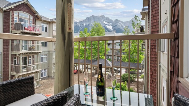 Ein Balkon mit Blick auf Berge, eine Champagnerflasche und zwei Gläser auf einem Glastisch.