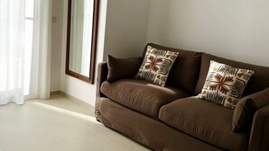 A living room with a brown sofa, two patterned cushions, a large mirror, and sheer curtains. - Appartamento in villa, 2 camere da letto e cucina (Bari)