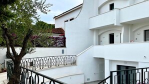 A modern white building with a curved facade, a metal railing, and a tree with purple flowers. - Appartamento in villa, 2 camere da letto e cucina (Bari)