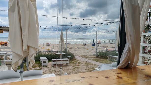 Uitzicht op het strand vanuit een kamer met een houten tafel, lichtslingers en strandparasols.