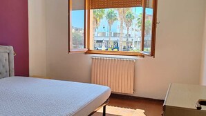 Een slaapkamer met een bed, een houten bureau, een raam met zonwering en een radiator.