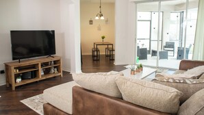 A living room with a flat-screen TV, wooden entertainment unit, beige sofa, and a dining area with a table and chairs. - 15 Mint to Disney 2 mint to the Best golf courses. Family size villa.      (Davenport)