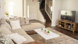 A spacious living room with a large sectional sofa, a white coffee table with potted plants, a wooden entertainment center with a flat-screen TV, and a staircase leading to an upper floor. - 15 Mint to Disney 2 mint to the Best golf courses. Family size villa.      (Davenport)