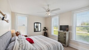 A bedroom with a bed, a dresser, a television, a ceiling fan, and large windows. - Country Charm on the Sandusky: Live Music Nearby (Fremont)
