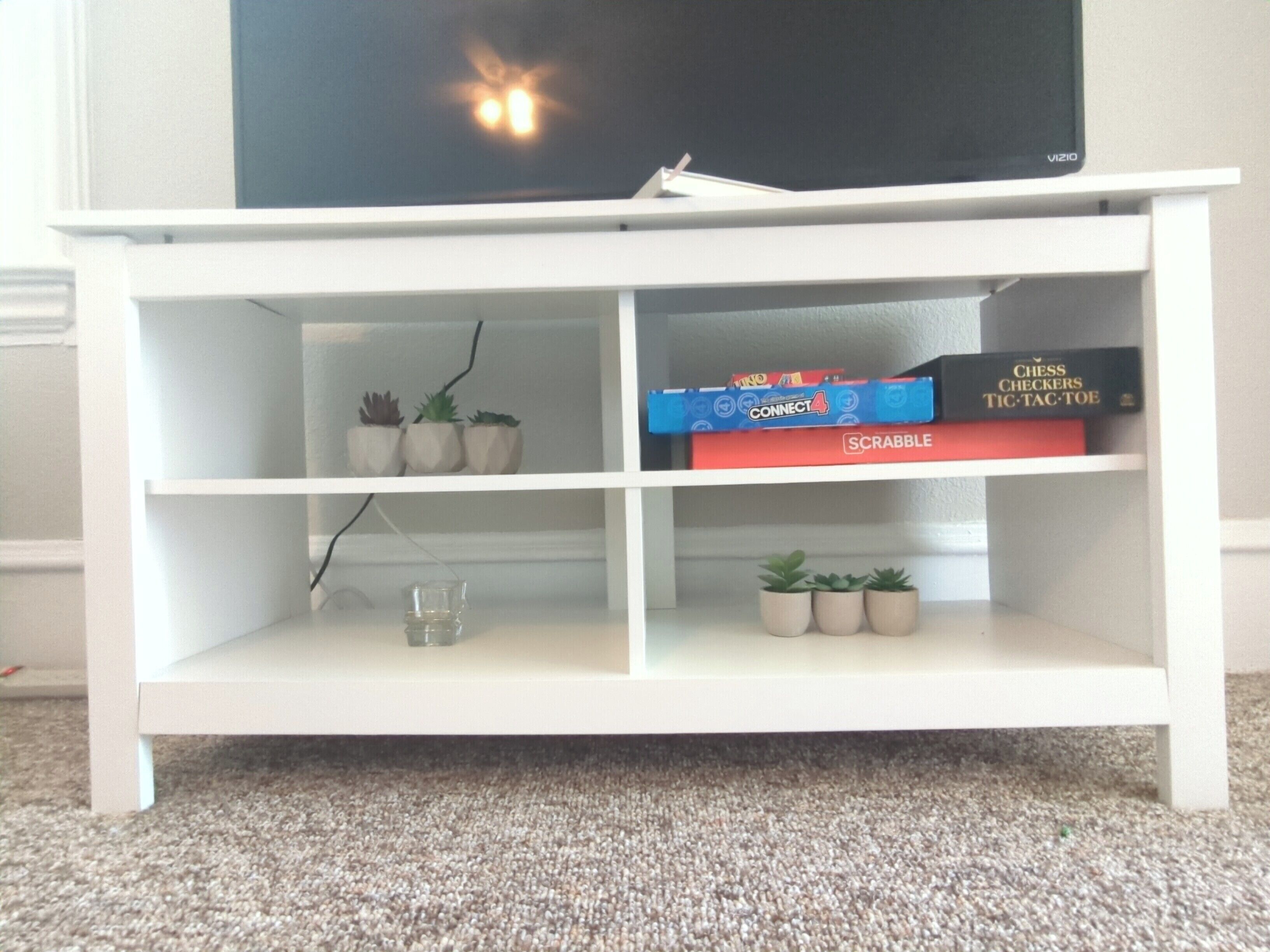 Een witte entertainmentkast met planken waarop bordspellen en een televisie staan.