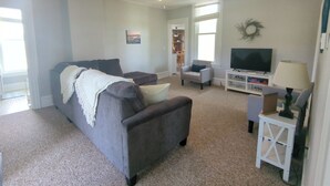 A living room with a grey sofa, a white side table, a television, and a ceiling fan. - Country Charm on the Sandusky: Live Music Nearby (Fremont)