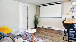 Ein Wohnzimmer mit Projektor, einer weißen Leinwand, einem Esstisch und einer Pflanze.