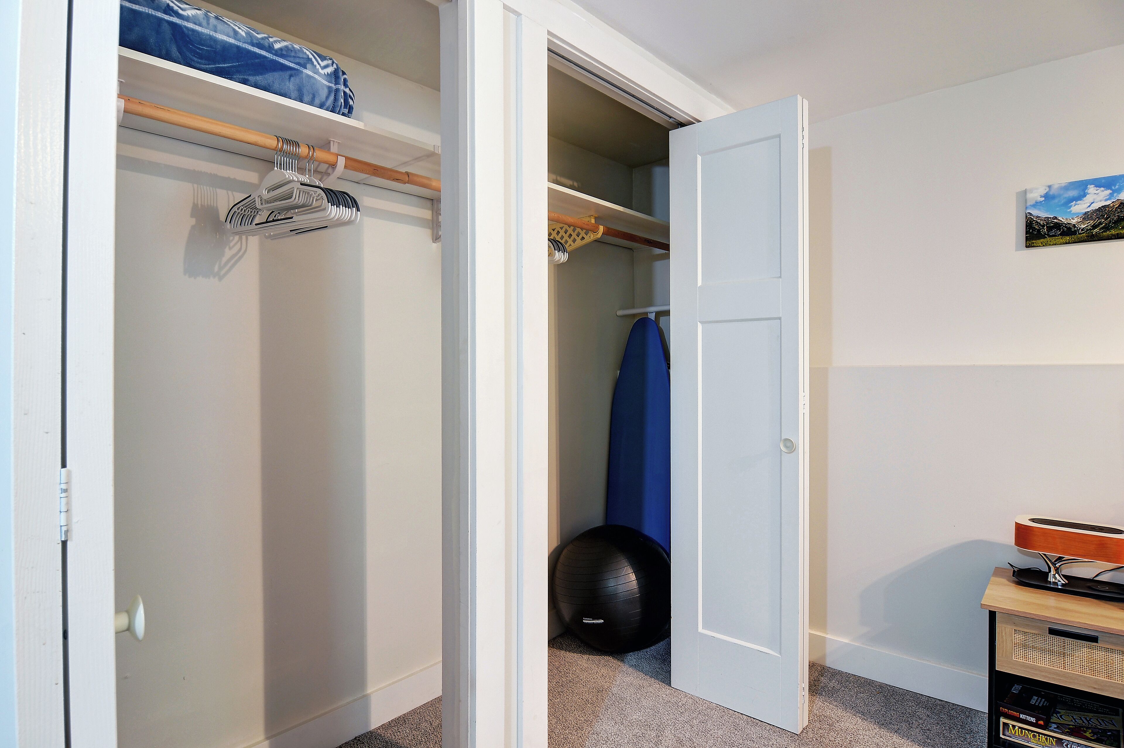 A room with a closet containing hanging clothes and a shelf with a blue bag.
