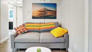 Ein Wohnzimmer mit grauem Sofa, bunten Kissen, einem Projektor an der Decke und einem großen Landschaftsbild an der Wand.