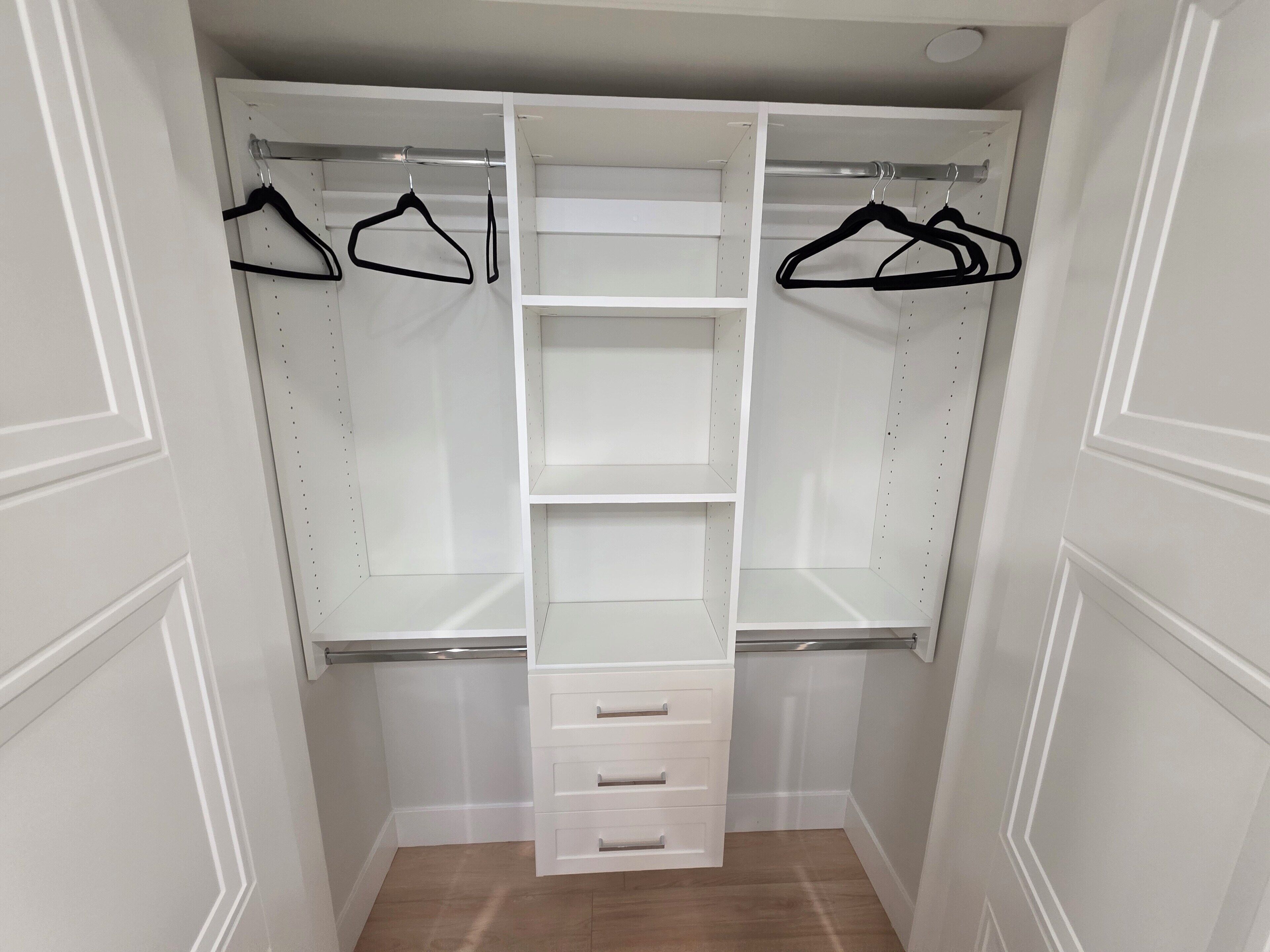 A walk-in closet with open shelves, hanging space, and a central drawer unit.
