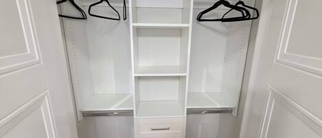 A walk-in closet with open shelves, hanging space, and a central drawer unit.
