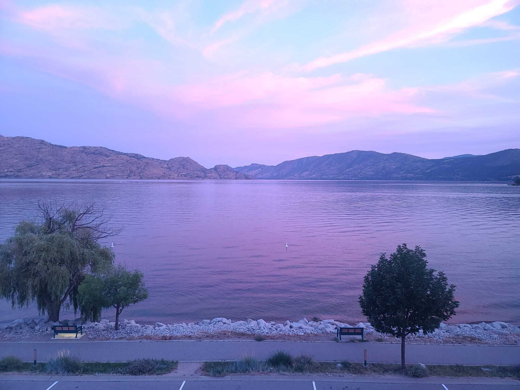 Un lac aux eaux calmes, entouré de collines et surplombé d’un ciel dégagé.