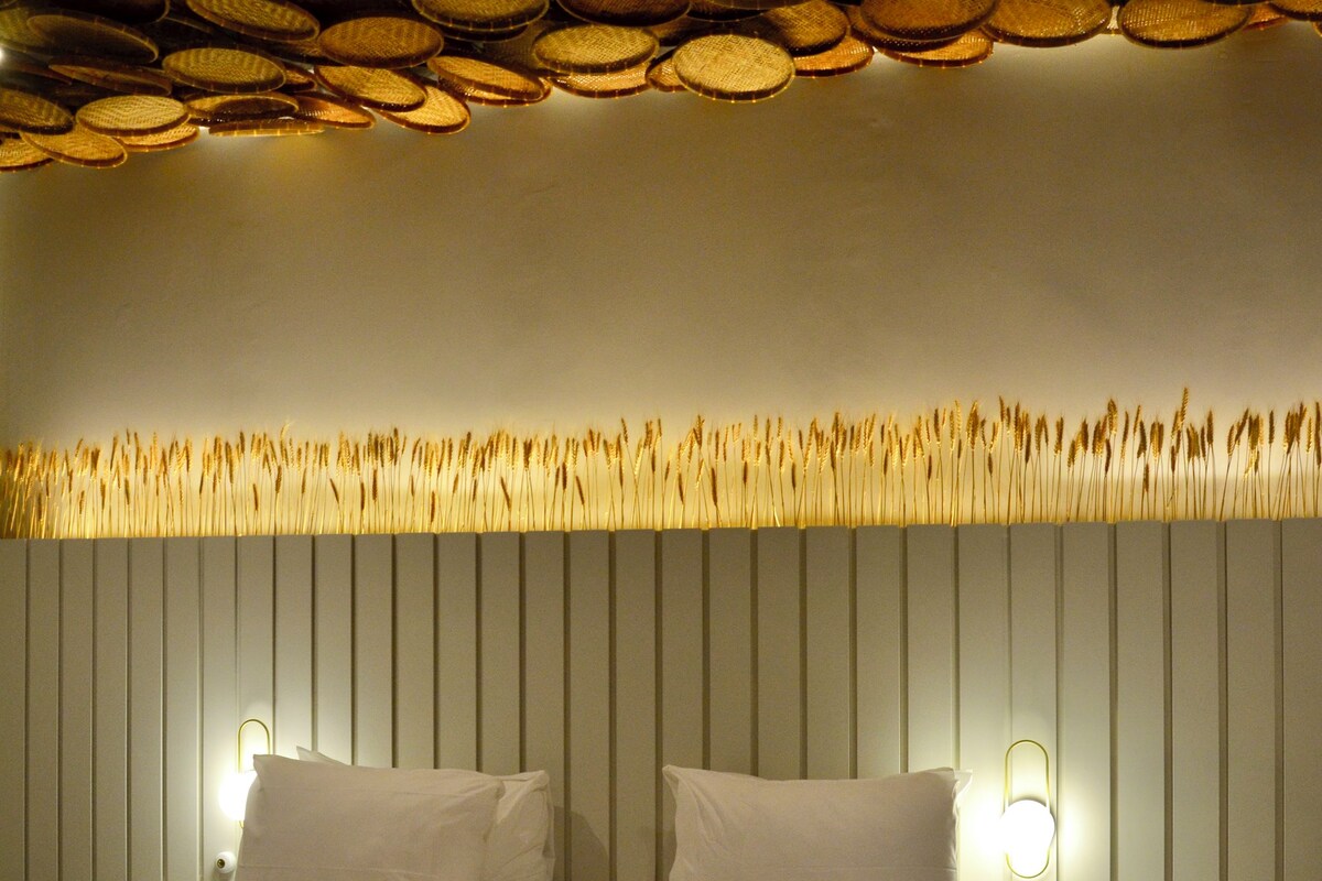 A neatly made bed with white linens and a rolled towel, a bedside table with a remote control, and a wall with a textured pattern above the bed.