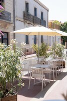 Mobiliario exterior con sombrillas, sillas blancas y plantas en macetas.