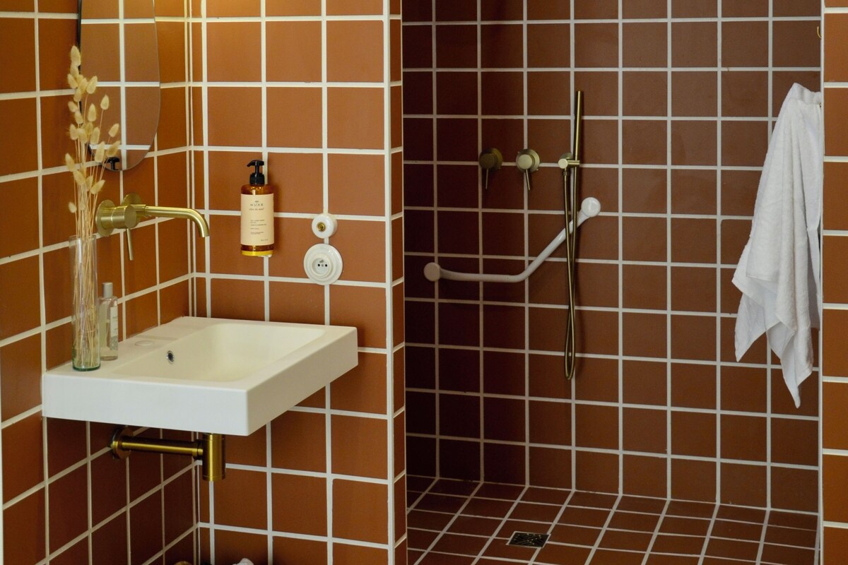 Un bagno con un lavandino bianco, uno specchio, una doccia e un porta asciugamani.