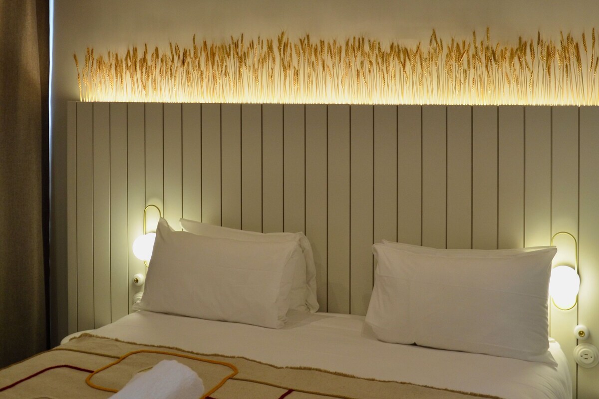 Hotelkamer met een bed, kussens, een opgerolde handdoek, een wandlamp en een plafond met geweven manden.