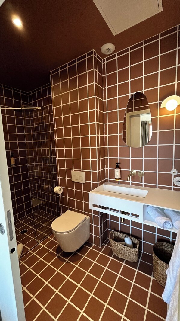 A bathroom with a tiled floor, a toilet, a sink with a mirror, and a shower area. - Maison Soleil (Montpellier)