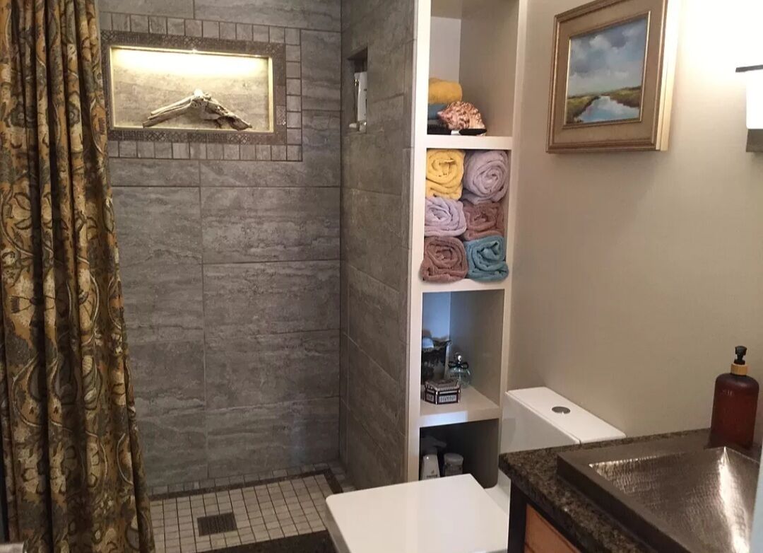 Un baño con ducha, inodoro, lavabo y repisas con toallas.