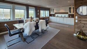 Een moderne keuken met witte kastjes, een eethoek met tafel en stoelen, en een grote klok aan de muur.