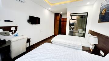 Habitación de hotel con dos camas, televisión, espejo, escritorio y baño visible a través de una puerta de cristal.