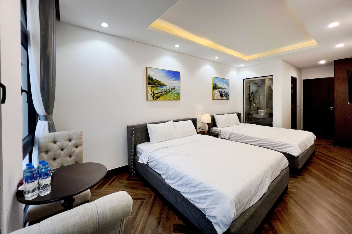 A hotel room with two beds, a small table with water bottles, a chair, and artwork on the walls.