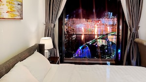 Een hotelkamer met een bed, nachtkastje, lamp en uitzicht op een felverlichte brug in de nacht.