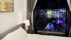 Hotelkamer met groot raam met uitzicht op een verlicht stadsbeeld bij nacht, inclusief gebouwen en een waterpartij.