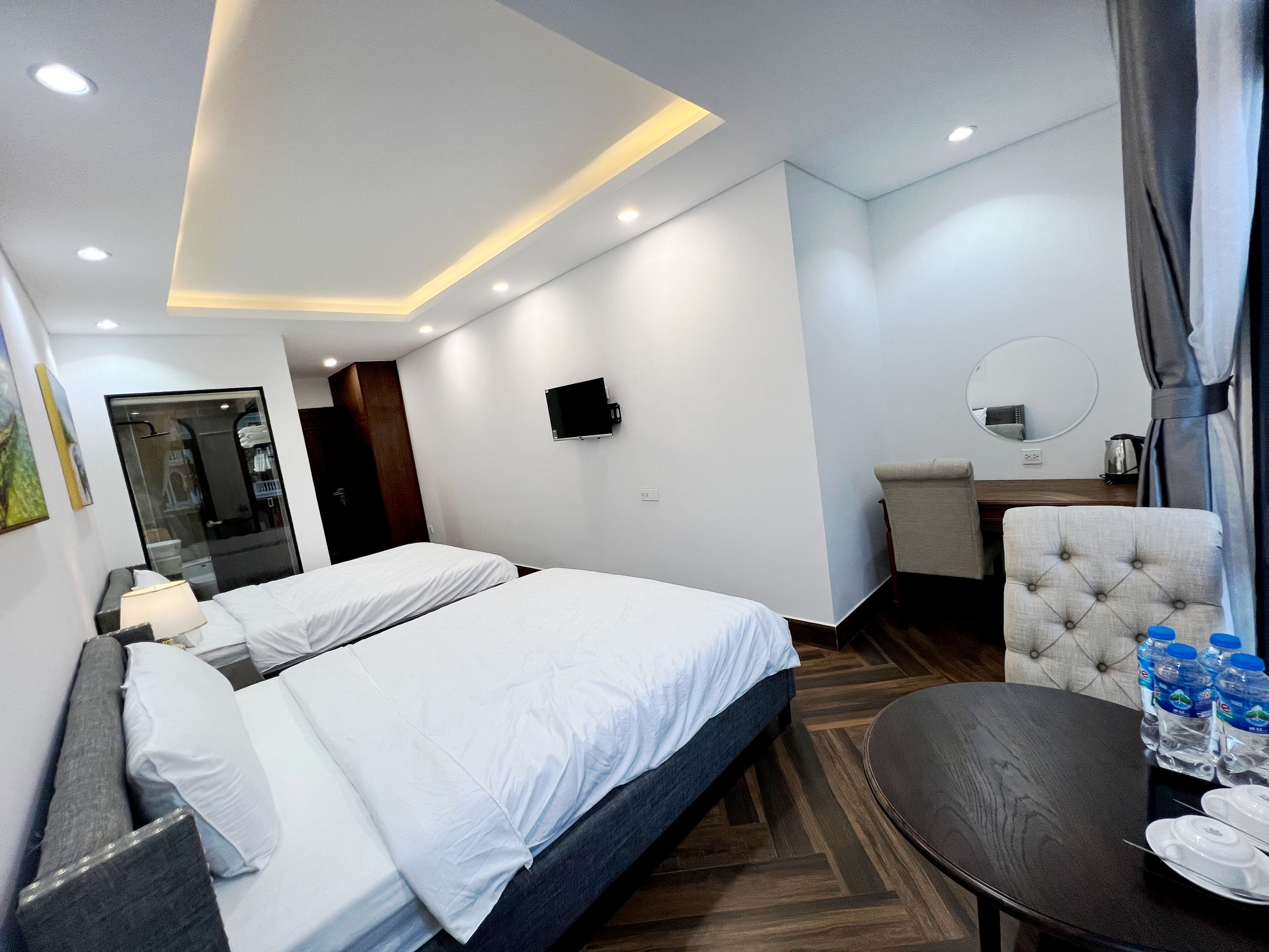 A hotel room with two beds, a desk, a chair, a mirror, and a table with water bottles.