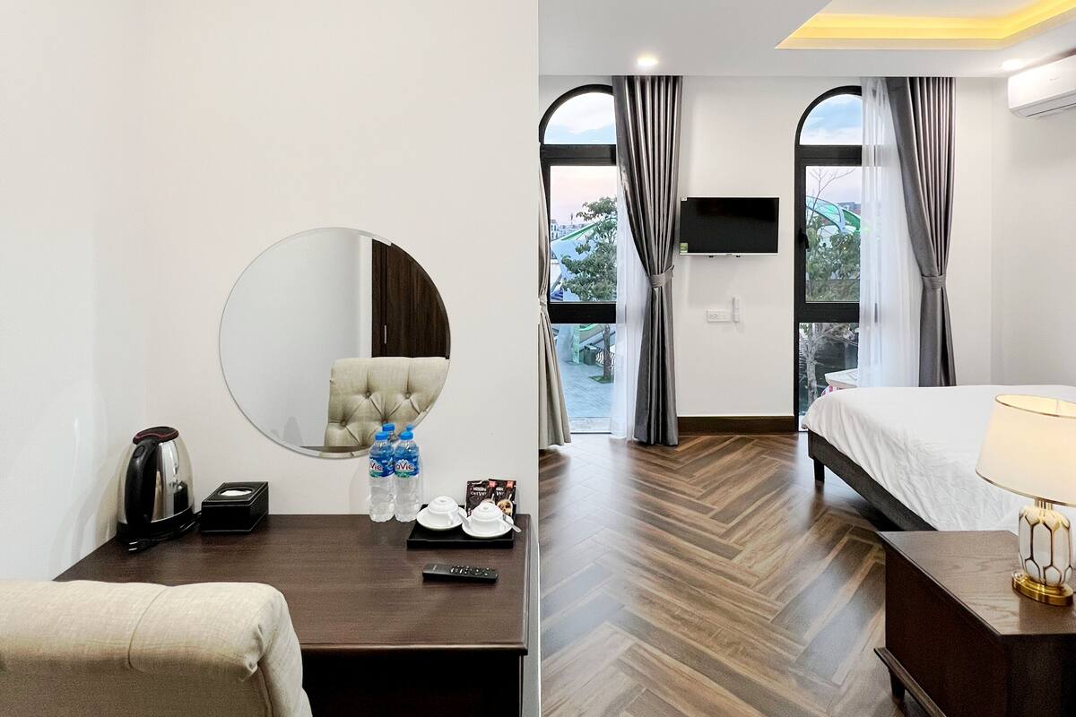 A hotel room with a bed, a desk with a mirror, a kettle, and a TV.