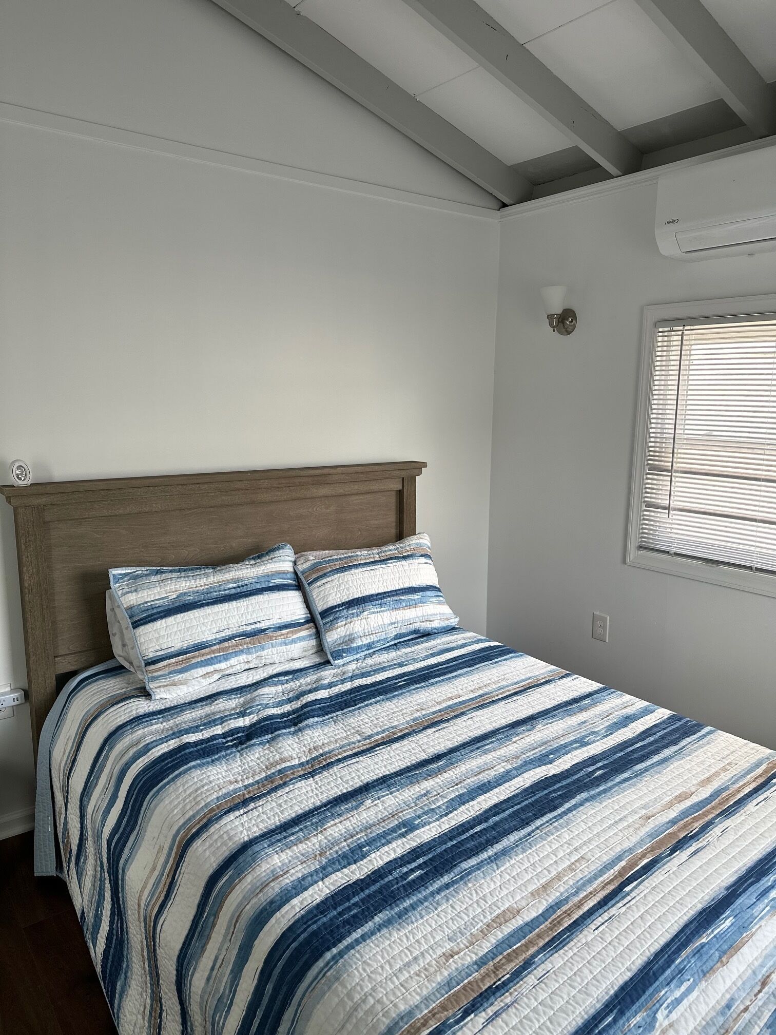A bedroom with a wooden headboard, a striped bedspread, and a window with blinds.