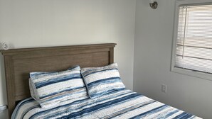 A bedroom with a wooden headboard, a striped bedspread, and a window with blinds. - Recently Renovated 3 Bedroom 1 Bath Clean Waterfront home with 50' Dock  (Stafford Township)