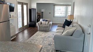 A spacious living area with a large sofa, a dining table, and a kitchen area with a refrigerator and a television. - Recently Renovated 3 Bedroom 1 Bath Clean Waterfront home with 50' Dock  (Stafford Township)