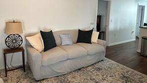A living room with a beige sofa, a patterned rug, and a lamp on a side table. - Recently Renovated 3 Bedroom 1 Bath Clean Waterfront home with 50' Dock  (Stafford Township)