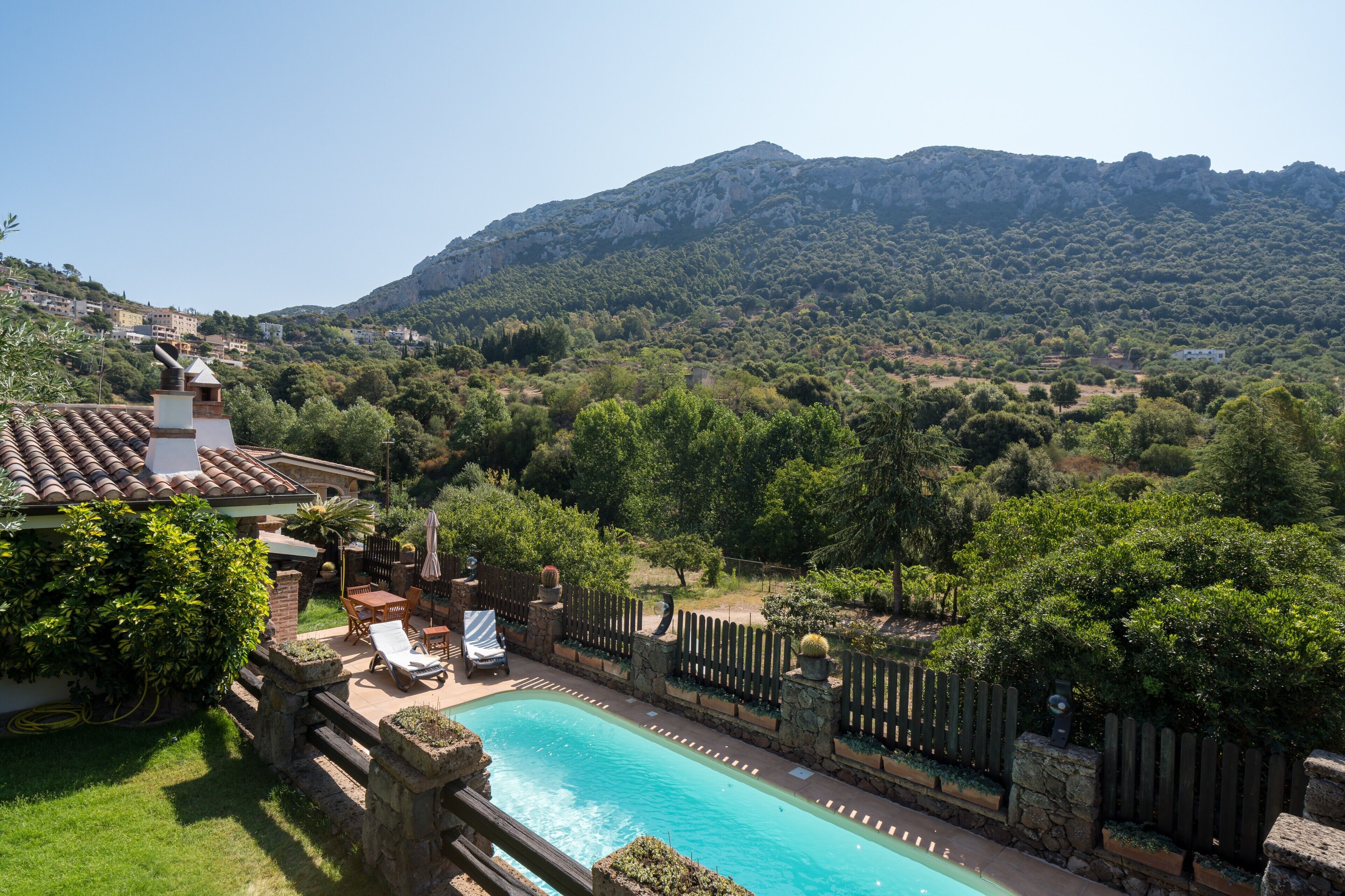 A swimming pool with a stone deck, surrounded by a wooden fence and lush greenery.