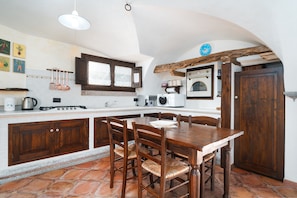 A kitchen with a dining table, wooden chairs, a stove, a microwave, and a clock on the wall. - Holiday Home 'Bados' with Mountain View, Pool & Air Conditioning (Dorgali)