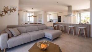A modern living room with a grey sectional sofa, a dining area with a table and chairs, a kitchen with white cabinets, and a bar area with stools. - Beautiful home in Son Macia (Son Macia)