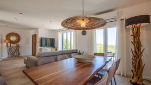 A modern dining area with a wooden table, cushioned seating, and a large woven light fixture. - Beautiful home in Son Macia (Son Macia)