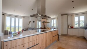 A modern kitchen with a central island, wooden cabinetry, and large windows offering a view of the outdoors. - Beautiful home in Son Macia (Son Macia)