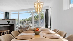 A modern dining area with a long table, multiple chairs, and a central bowl of fruit.