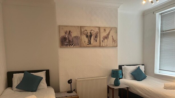 Une chambre avec deux lits, un radiateur, une lampe et des œuvres d’art accrochées au mur.