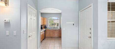 Un estrecho pasillo que conduce a una cocina con armarios de madera, una ventana con persianas y una puerta a la derecha.