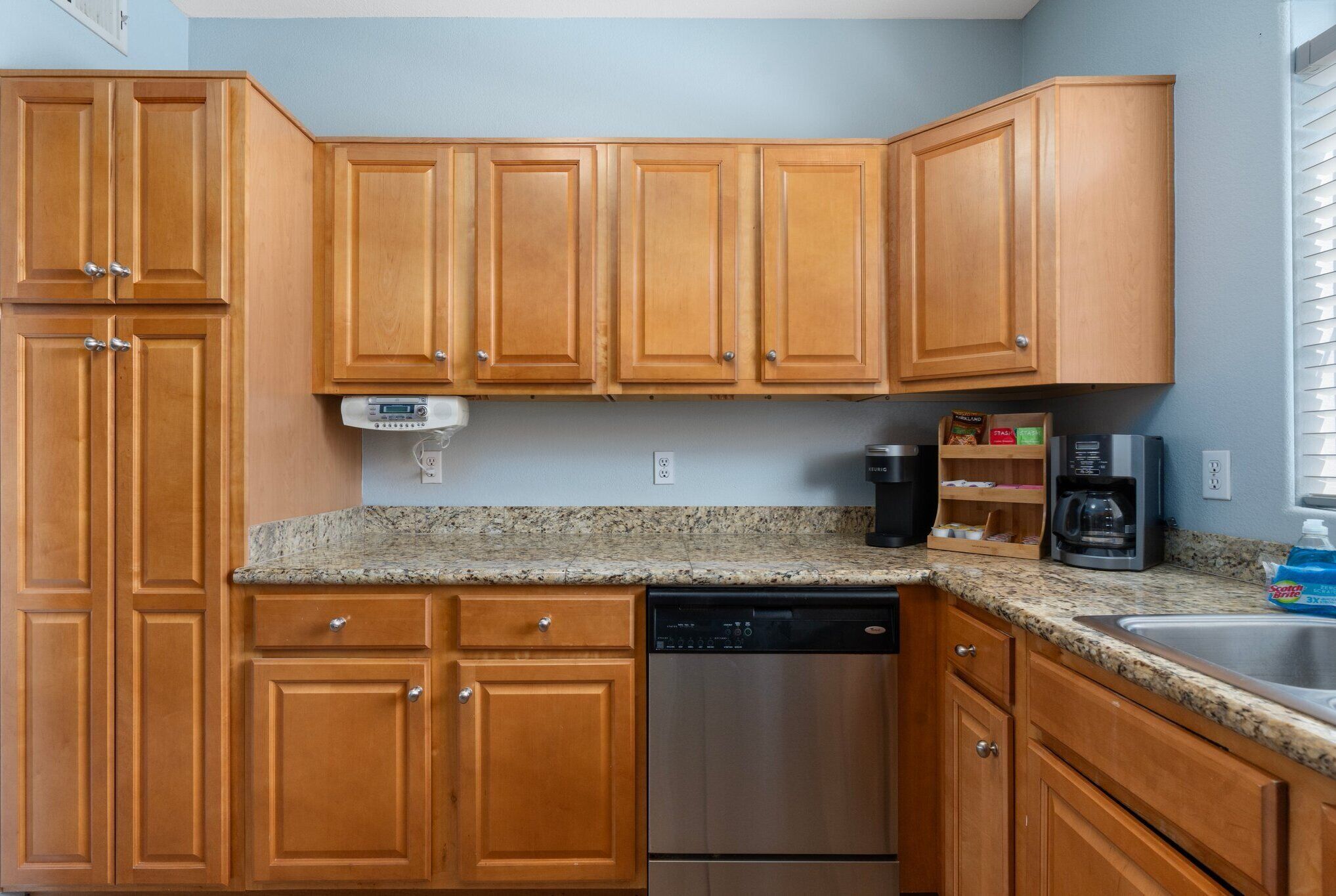 A kitchen with wooden cabinets, a dishwasher, a coffee maker, and a granite countertop.