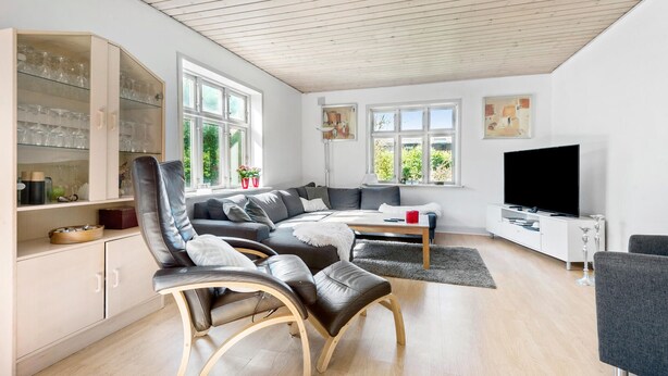 Een moderne woonkamer met een bank, stoelen, een televisie en een glazen kast met wijnglazen.
