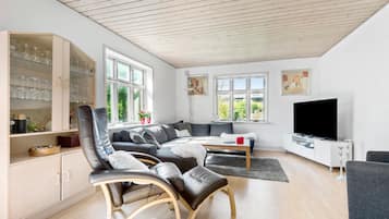 Un salon moderne comprenant un canapé, des fauteuils, un téléviseur et un meuble vitré contenant des verres à vin.