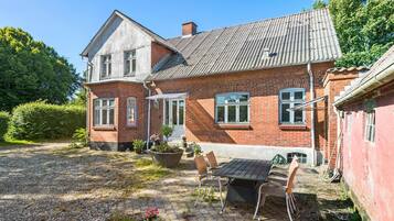 Une maison à deux étages, construite en briques, avec un toit en pente, un porche à l’avant et une allée gravillonnée.
