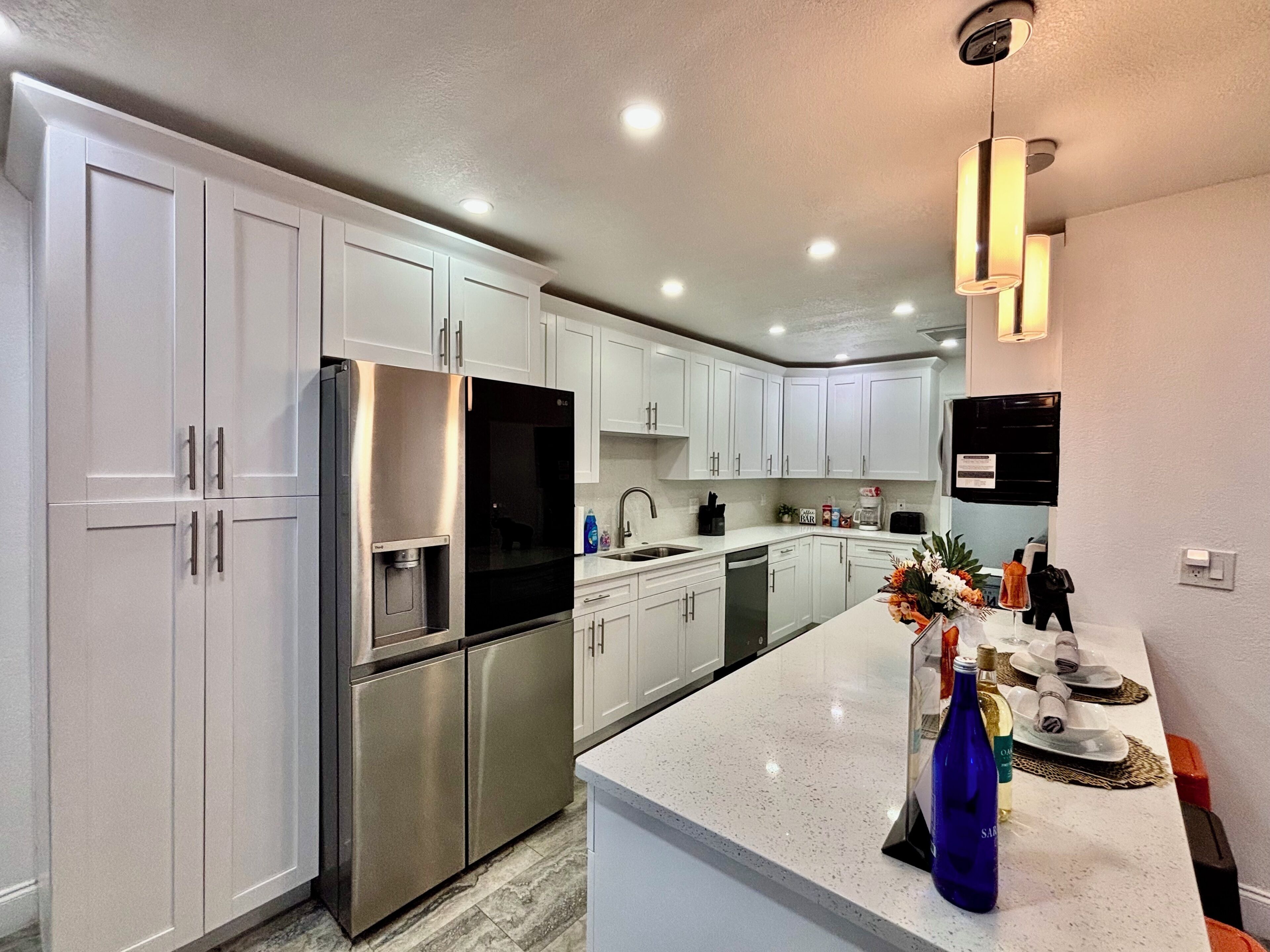 A modern kitchen with white cabinetry, stainless steel appliances, and a central island with a vase and bottles.